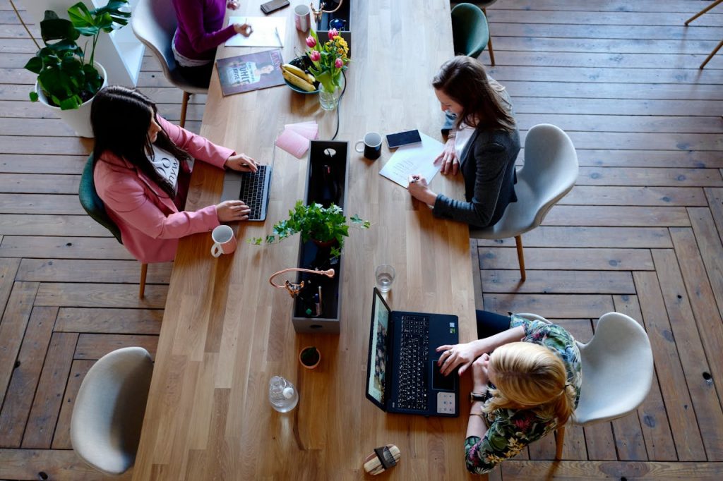 Women working in a coworking space and sitting around the same long desk.