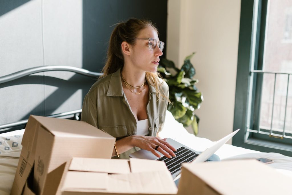 woman typing on laptop among cardboard boxes