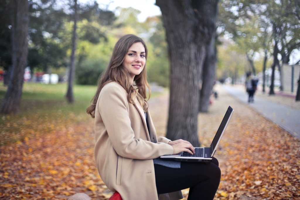 A woman typing on a laptop in a park.
