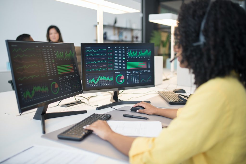 Woman in yellow long-sleeve shirt looking at computer data.