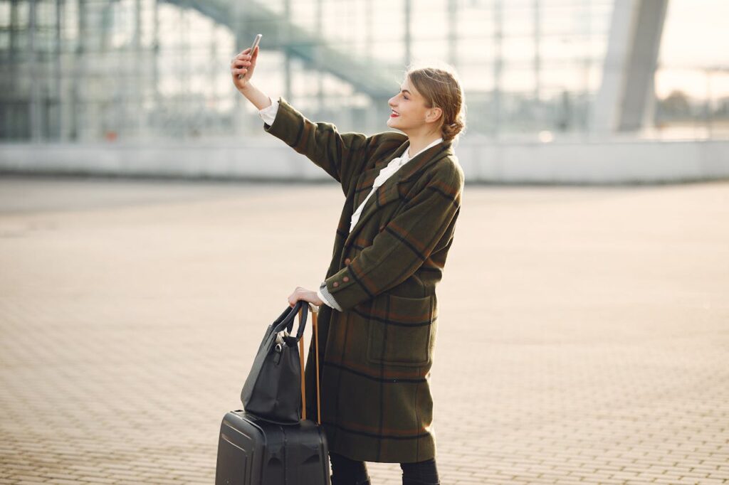 Stylish young woman with luggage taking a selfie